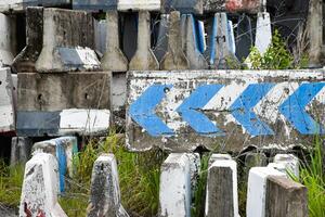 Old concrete road barrier with blue directional arrows is abandoned at a junkyard as a concrete block used to block roads and traffic. Many concrete barriers are old and decayed. photo