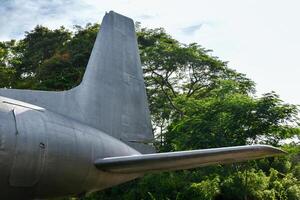 The tail of an old airplane showing the rusting steel surface and the airplane's emergency exit door on a forest and sky background. photo