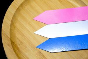 Close-up three plastic name tags in blue, white and pink for plant names or to add text are placed on beautifully patterned wooden plates over a black background. photo