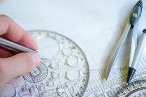 Engineer's hand holding a pencil with circle ruler and sketching a house plan for pre-construction plans on white paper with dividers for interior and architectural design concept. photo