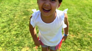 A small child runs cheerfully along a green lawn, surrounded by bright flowers and tall trees, their shadows sheltering him from the warm summer sun. video