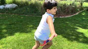 A small child runs cheerfully along a green lawn, surrounded by bright flowers and tall trees, their shadows sheltering him from the warm summer sun. video