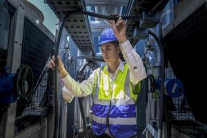 An industrial worker in high-visibility gear and a blue helmet meticulously examines the intricate network of machinery. The engineer is dedicated to maintaining operational efficiency and safety. photo