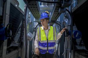 An industrial worker in high-visibility gear and a blue helmet meticulously examines the intricate network of machinery. The engineer is dedicated to maintaining operational efficiency and safety. photo