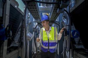 An industrial worker in high-visibility gear and a blue helmet meticulously examines the intricate network of machinery. The engineer is dedicated to maintaining operational efficiency and safety. photo