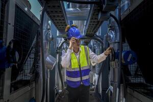 An industrial worker in high-visibility gear and a blue helmet meticulously examines the intricate network of machinery. The engineer is dedicated to maintaining operational efficiency and safety. photo