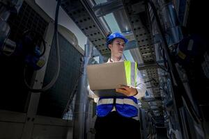 An industrial worker in high-visibility gear and a blue helmet meticulously examines the intricate network of machinery. The engineer is dedicated to maintaining operational efficiency and safety. photo
