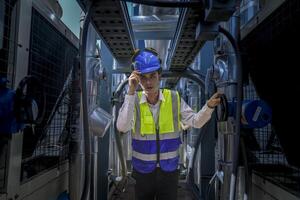 An industrial worker in high-visibility gear and a blue helmet meticulously examines the intricate network of machinery. The engineer is dedicated to maintaining operational efficiency and safety. photo