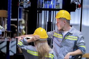 Two male and female factory checkers are discussing work on a warehouse truck. While working in a warehouse for industrial products photo