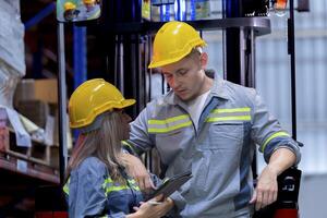Two male and female factory checkers are discussing work on a warehouse truck. While working in a warehouse for industrial products photo
