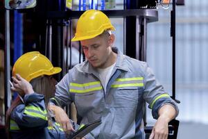 Two male and female factory checkers are discussing work on a warehouse truck. While working in a warehouse for industrial products photo