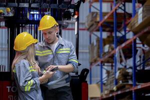 Two male and female factory checkers are discussing work on a warehouse truck. While working in a warehouse for industrial products photo