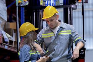 Two male and female factory checkers are discussing work on a warehouse truck. While working in a warehouse for industrial products photo