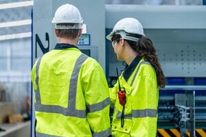 Male and female engineers in neat work clothes prepare and control the production system of large modern machines in a factory producing industrial technology products. photo