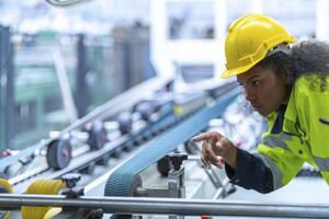 Portrait of African woman worker beautiful face with eye confident and wearing working suite dress and safety helmet at heavy machine in industry factory. Engineer worker concentrate on workplace. photo