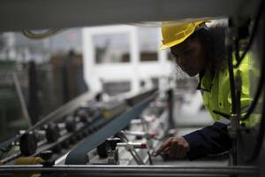 Portrait of African woman worker beautiful face with eye confident and wearing working suite dress and safety helmet at heavy machine in industry factory. Engineer worker concentrate on workplace. photo