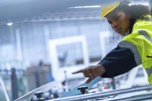 Portrait of African woman worker beautiful face with eye confident and wearing working suite dress and safety helmet at heavy machine in industry factory. Engineer worker concentrate on workplace. photo