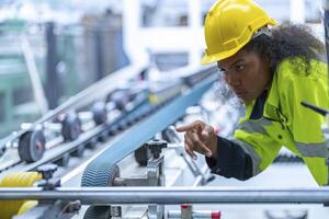 Portrait of African woman worker beautiful face with eye confident and wearing working suite dress and safety helmet at heavy machine in industry factory. Engineer worker concentrate on workplace. photo