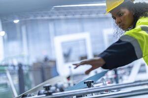 Portrait of African woman worker beautiful face with eye confident and wearing working suite dress and safety helmet at heavy machine in industry factory. Engineer worker concentrate on workplace. photo