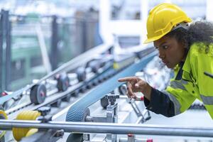 Portrait of African woman worker beautiful face with eye confident and wearing working suite dress and safety helmet at heavy machine in industry factory. Engineer worker concentrate on workplace. photo