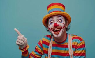 Happy Clown Wearing Striped Shirt and Hat Pointing With Finger Against Blue Background photo