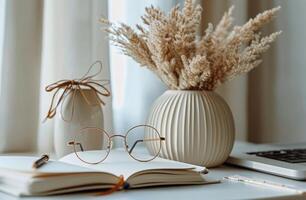 Open Notebook With Glasses and Dried Flowers in Vase on White Desk photo