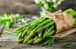 Fresh Green Asparagus Spears Wrapped in Brown Paper on Rustic Wooden Surface photo