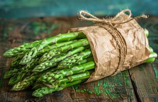 Fresh Green Asparagus Spears Wrapped in Brown Paper on Rustic Wooden Surface photo