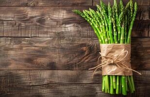Fresh Green Asparagus Spears Wrapped in Brown Paper on Rustic Wooden Surface photo