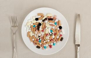 Plate of pills fork and knife next to it. Concept of excessive consumption of drugs that replace healthy diet. photo