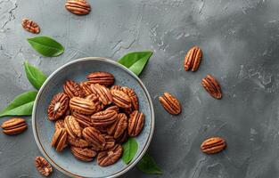 Bowl of Shelled Pecans With Green Leaves on a Gray Surface photo