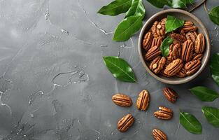Bowl of Shelled Pecans With Green Leaves on a Gray Surface photo