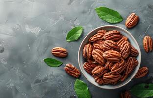 Bowl of Shelled Pecans With Green Leaves on a Gray Surface photo