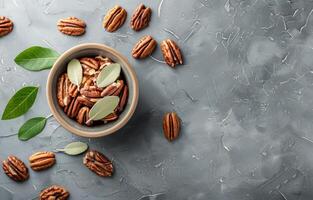 Bowl of Shelled Pecans With Green Leaves on a Gray Surface photo
