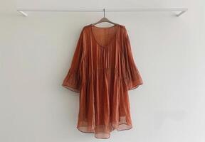 Rust Colored Sheer Blouse With Bell Sleeves Hanging on a White Hanger photo