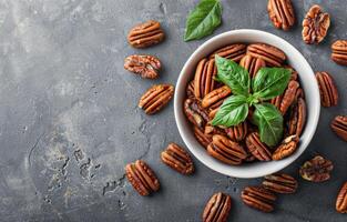 Bowl of Pecan Nuts With Green Leaves on a Grey Surface photo