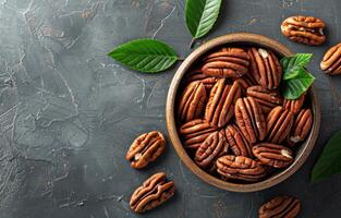 Bowl of Pecan Nuts With Green Leaves on a Grey Surface photo