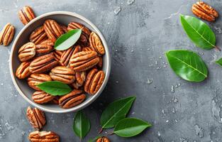 Bowl of Pecan Nuts With Green Leaves on a Grey Surface photo