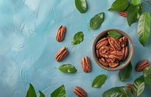 Bowl of Pecan Nuts With Green Leaves on a Blue Background photo