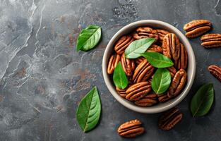 Bowl of Pecan Nuts With Green Leaves on a Grey Surface photo