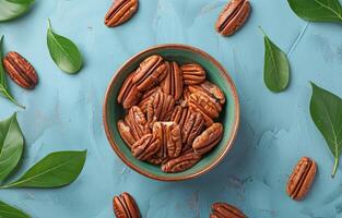 Bowl of Pecan Nuts With Green Leaves on a Blue Background photo