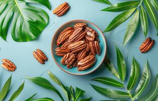 Bowl of Pecan Nuts With Green Leaves on a Blue Background photo