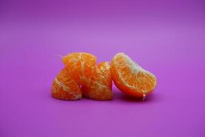 oranges that have been peeled and divided into several parts. orange isolated on purple background photo