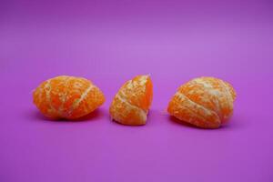 oranges that have been peeled and divided into several parts. orange isolated on purple background photo