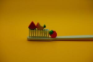 white toothbrush with fruit toys on it. White toothbrush isolated on dark yellow background photo