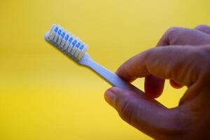hand holding a white toothbrush. White toothbrush isolated on yellow background. photo