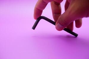 hand holding an L key. Allen key isolated on purple background photo