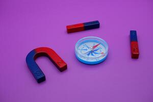 a compass, 2 bar magnets, and a horseshoe magnet isolated on a purple background photo