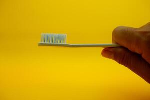 hand holding a white toothbrush. White toothbrush isolated on yellow background. photo