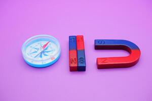 a compass, 2 bar magnets, and a horseshoe magnet isolated on a purple background photo